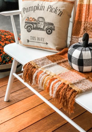 White bench with fall pillows, a blanket and a pumpkin