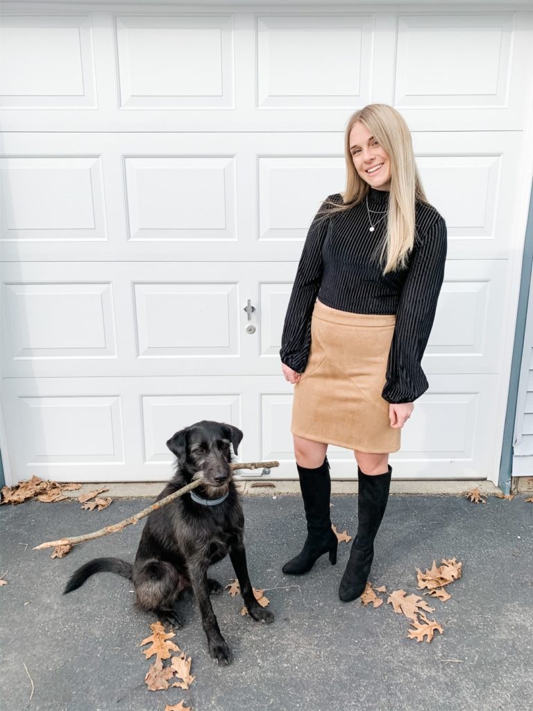 Girl in crop top, skirt, black boots and dog in front of garage