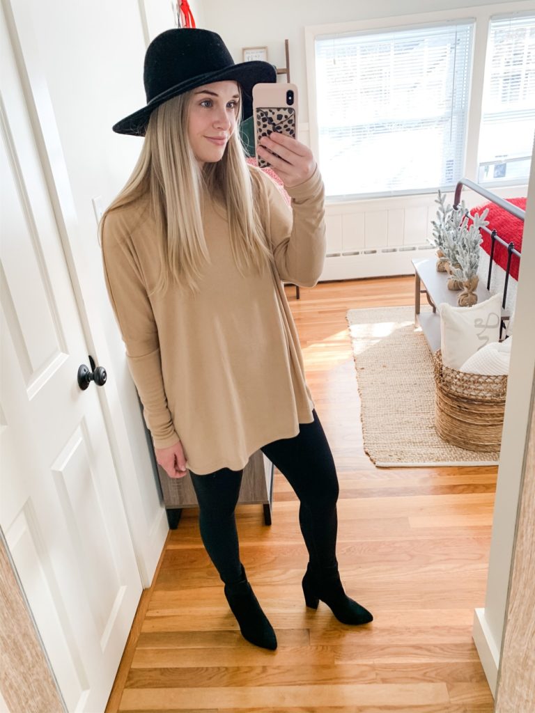 Girl with oversized tan tunic, black hat, leggings and black boots