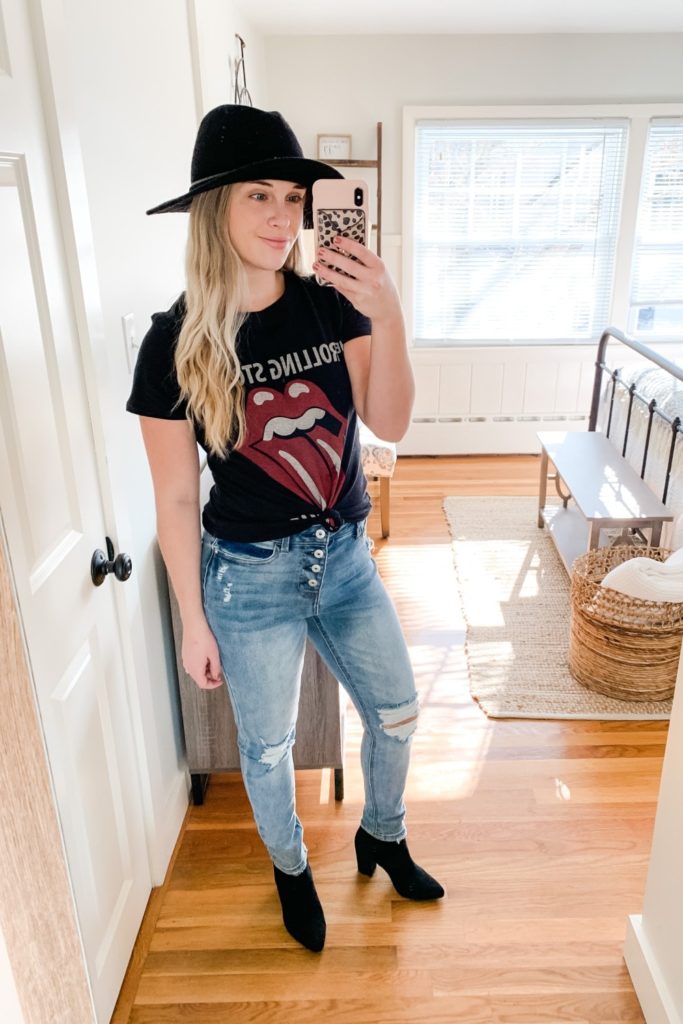 Girl in a rolling stones shirt. a black hat, distressed jeans and Black booties