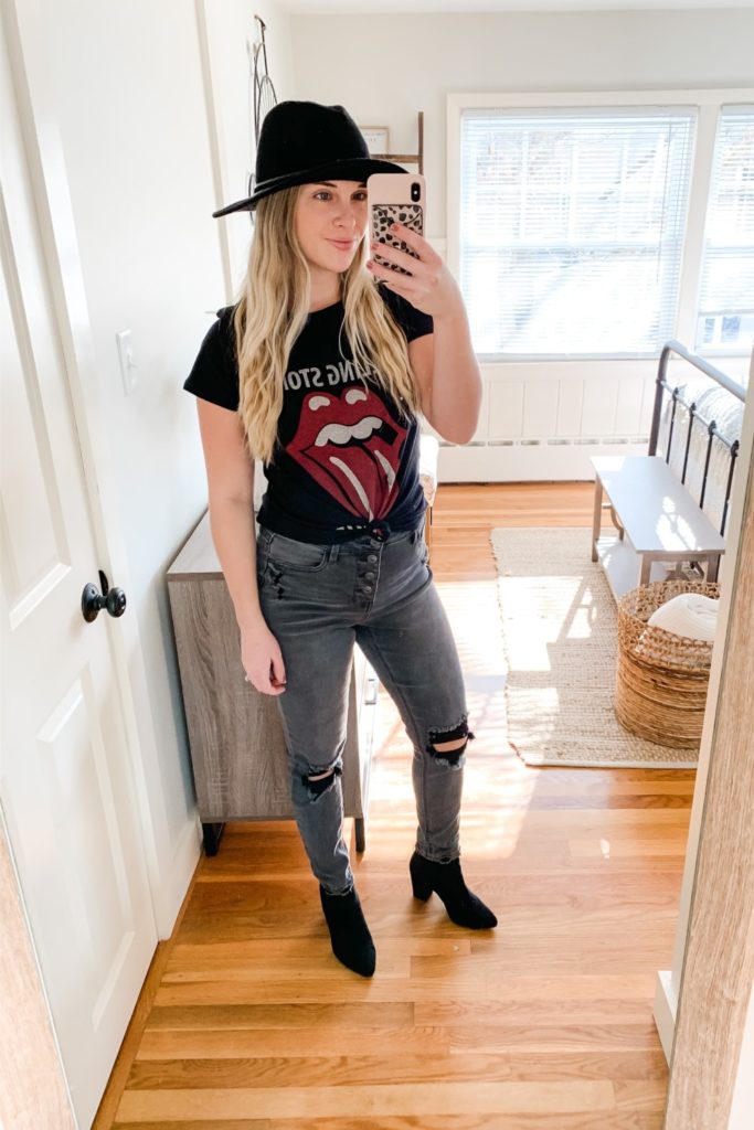 Girl in a rolling stones shirt. a black hat, black distressed jeans and Black booties